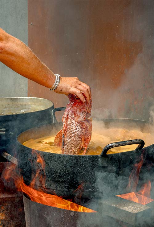 Cuisson de la bouillabaisse au feu de bois au restaurant L'Aventure à Carqueiranne — poisson frais plongé à la main dans le bouillon